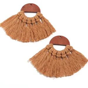 Gros plan détaillé des boucles d'oreilles bohèmes à franges en coton et demi-cercle en bois.