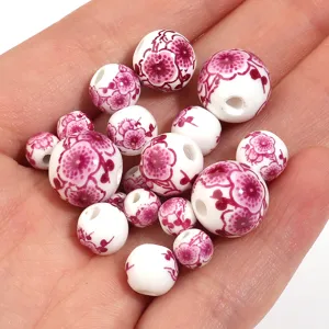 Primo piano di perline in ceramica bianca con motivi floreali rosa, ideali per gioielli fai da te.