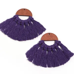Boucles d'oreilles bohèmes en bois demi-cercle et pompons en coton violet gros plan.