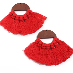 Gros plan sur les boucles d'oreilles à franges en bois, détail de bijoux en fil de coton rouge.