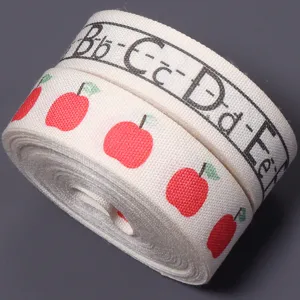 Close-up detail view of cream cotton ribbon featuring cute red apple print and alphabet.