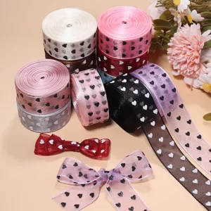 Primo piano di nastri in satin e organza con stampa a cuori e fiocchi per progetti fai da te e decori.