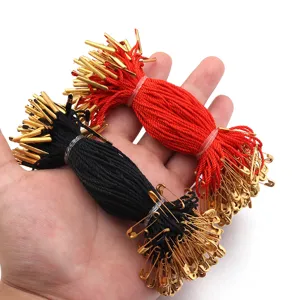 Detail view of clothing hang tag strings with gold safety pins, red and black cords bundle.