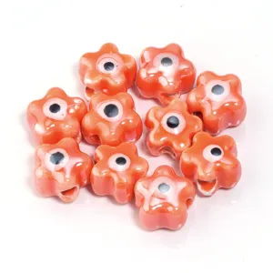 Close-up detailweergave van oranje keramische bloemkralen met boze oog motief voor DIY sieraden.