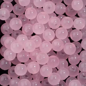 Gros plan détaillé de perles de verre rondes roses avec trous pour fabrication de bijoux DIY.