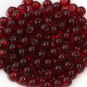 Gros plan detaille de perles rondes en verre rouge fonce pour la creation de bijoux faits main.