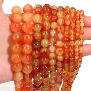 Primo piano di perle tonde in agata arancione viva, pietre sfuse multi-misura per gioielli.