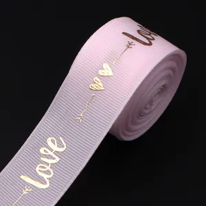 Pink polyester grosgrain ribbon featuring metallic gold love and heart print detail close up.