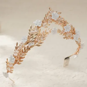 Accessoire de cheveux de mariée doré avec fleurs en céramique blanche et feuilles en cristal.