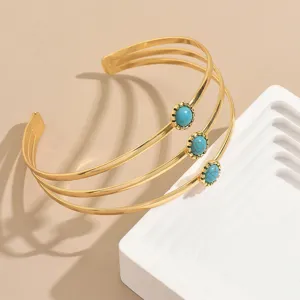 Primo piano dettagliato di un bracciale da braccio dorato multistrato con pietre turchesi.