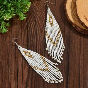 Dettaglio orecchini con frange di perline bianco e oro, stile etnico boho geometrico e chic.