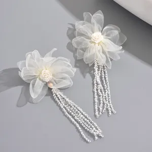Nahaufnahme eleganter weißer Spitzenblumen-Ohrringe mit langen Perlen-Fransenquasten.