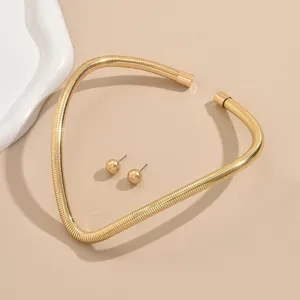 Gros plan détaillé du set de collier ras-de-cou souple et de boucles d'oreilles géométrique doré.