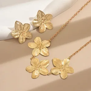 Detailaufnahme von goldenem Blumenschmuck mit metallischen Ohrringen und passender Kette.