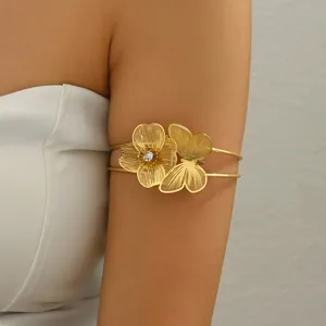 Primo piano del bracciale da braccio dorato con fiore strutturato, farfalla e strass.