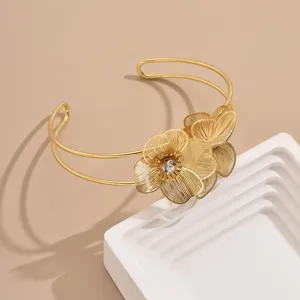 Primo piano dettagliato del bracciale rigido dorato con fiori in filigrana e cristallo.