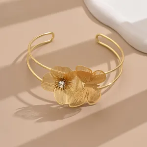 Primo piano dettagliato del bracciale rigido aperto dorato con fiori e farfalle.