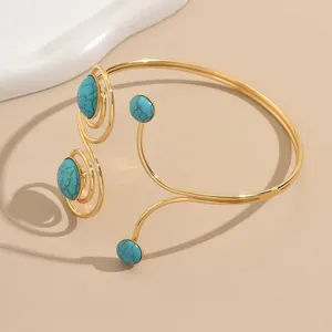 Bracciale da braccio aperto dorato con design geometrico traforato e pietre turchesi.