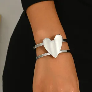 Close-up detail of the silver double-band cuff bracelet with a large heart charm on wrist.
