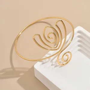 Vista dettagliata del bracciale in metallo dorato con un design a spirale geometrica astratta.