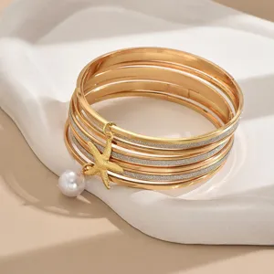 Gros plan sur un ensemble de 7 bracelets dorés multicouches avec étoile de mer et perle.