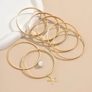 Vue détaillée d'un ensemble de 7 bracelets dorés élégants avec pendentifs perle et étoile de mer.