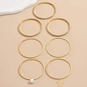 Ensemble de 7 joncs dorés avec pendentifs perle et étoile de mer et finitions pailletées.