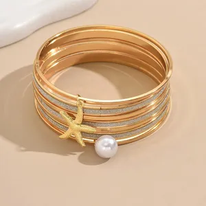 Ensemble de bracelets empilés multicouches dorés avec de délicats pendentifs étoile de mer et perle.