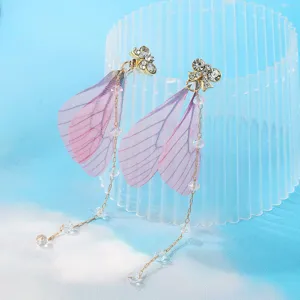 Primo piano dettagliato di orecchini con fiocco in strass e delicate ali di fata rosa.