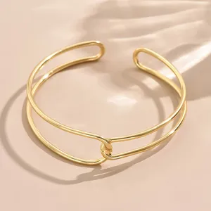 Primo piano dettagliato del bracciale aperto geometrico minimalista in metallo dorato.