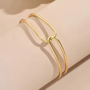 Primo piano dettaglio di un bracciale da braccio geometrico aperto dorato con texture metallica.