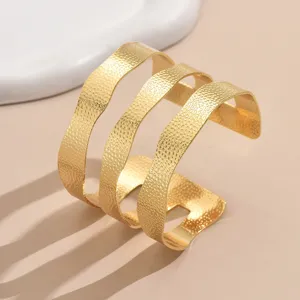 Bracelet manchette multicouche doré à motif ondulé, design géométrique texturé, détail métal.