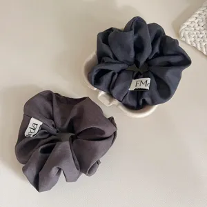 Detailopname van donkergrijze stoffen haarelastiekjes met kleine etiketten op tafel.