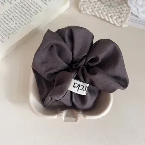 Minimalistische donkergrijze stoffen haarelastiek met klein label, zacht haaraccessoire.