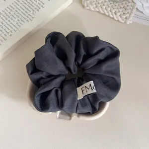 Close-up van een donkergrijze stoffen haarscrunchie met een klein minimalistisch labeldetail.