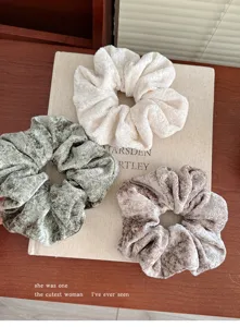 Detailaufnahme von weichen Plüsch-Haargummis in Creme, Olivgrün und Braun, flauschig.