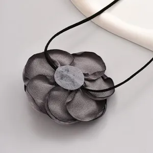 Gros plan détail d'un collier pendentif fleur en tissu gris foncé sur fond gris simple.