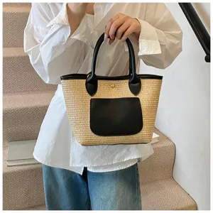 Detailed view of the woven straw bucket bag with black leather handle and front pocket design.