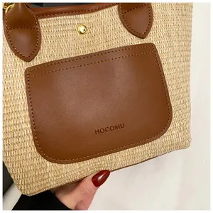 Detailed view of the straw woven handbag featuring brown leather pocket and gold tone hardware.