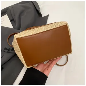 Detailed shot of trendy straw bucket bag featuring brown leather base and adjustable strap.