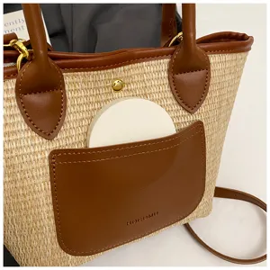Close-up detail view of the straw woven crossbody bag pocket and brown leather handle texture.