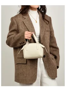 Primo piano di una borsa a mano minimalista in pelle beige retta da modella, stile chic.