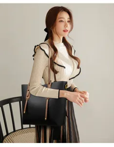Detail view of a black tote bag carried by a model, featuring brown straps and texture.