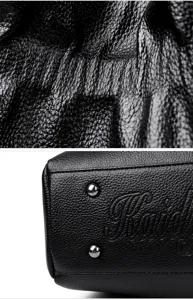 Detailed closeup view of black leather texture and metal protective feet on a handbag.