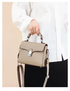 Detail view of a genuine leather taupe crossbody bag with metal lock and top handle.