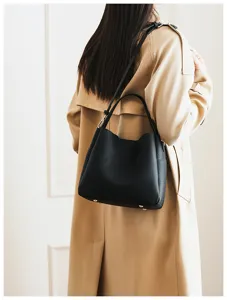 Close-up shot of a classic black soft leather bucket bag worn by a model indoors.