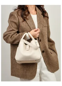 Gros plan détaillé d'un sac seau élégant en cuir beige texturé tenu par un mannequin.