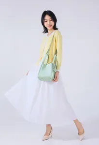 Detailed view of a stylish light green bucket handbag paired with a yellow cardigan and skirt.