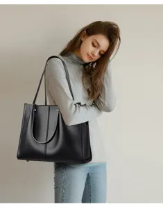 Detail shot of a black leather tote bag with wide strap, showcasing the shoulder carry style.
