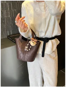 Dettaglio elegante della borsa a secchiello marrone con ciondolo orsetto e chiusura in metallo.